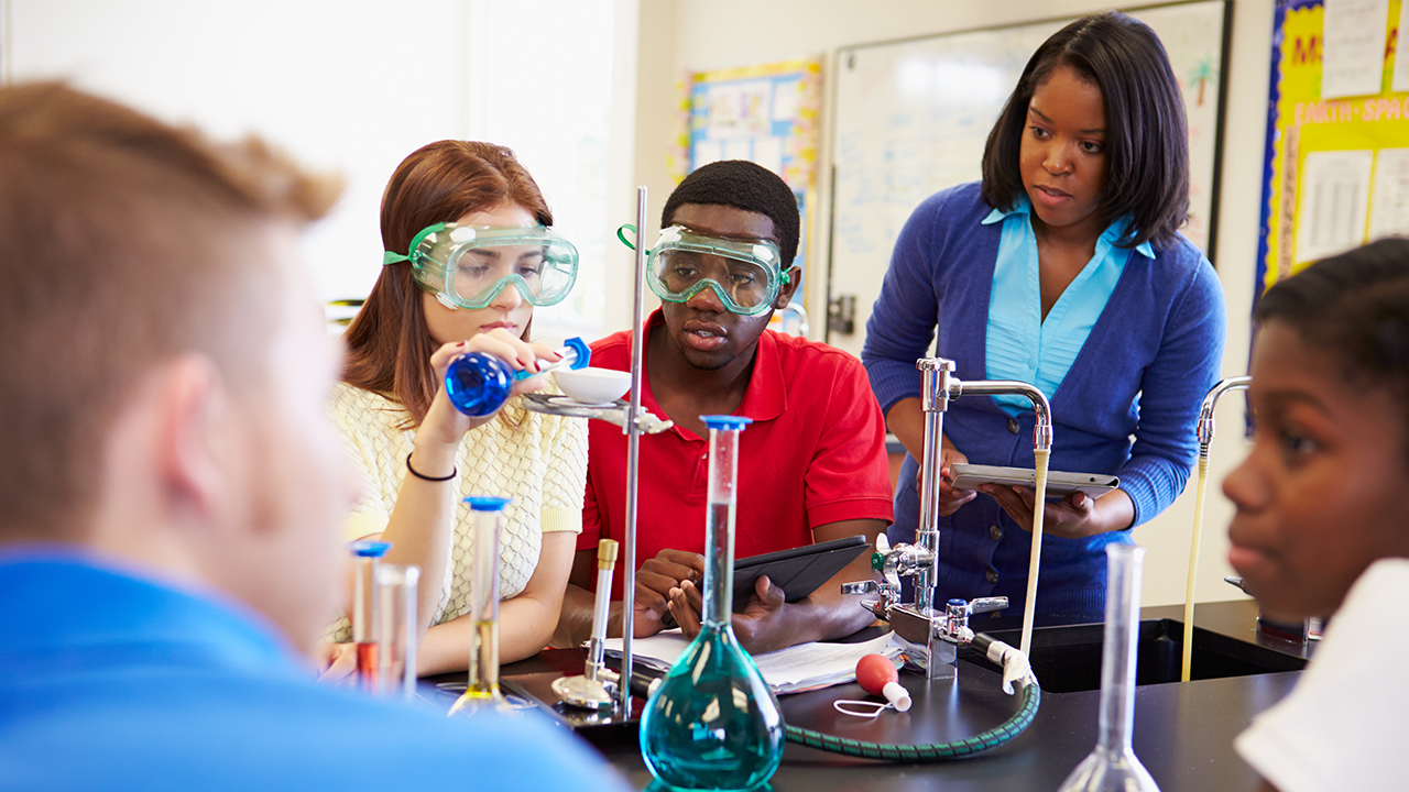 Highschool students in a science class setting, mixing test tubes.