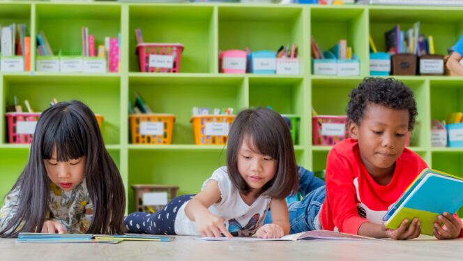 Group of diverse children laying on a classroom floor reading books.