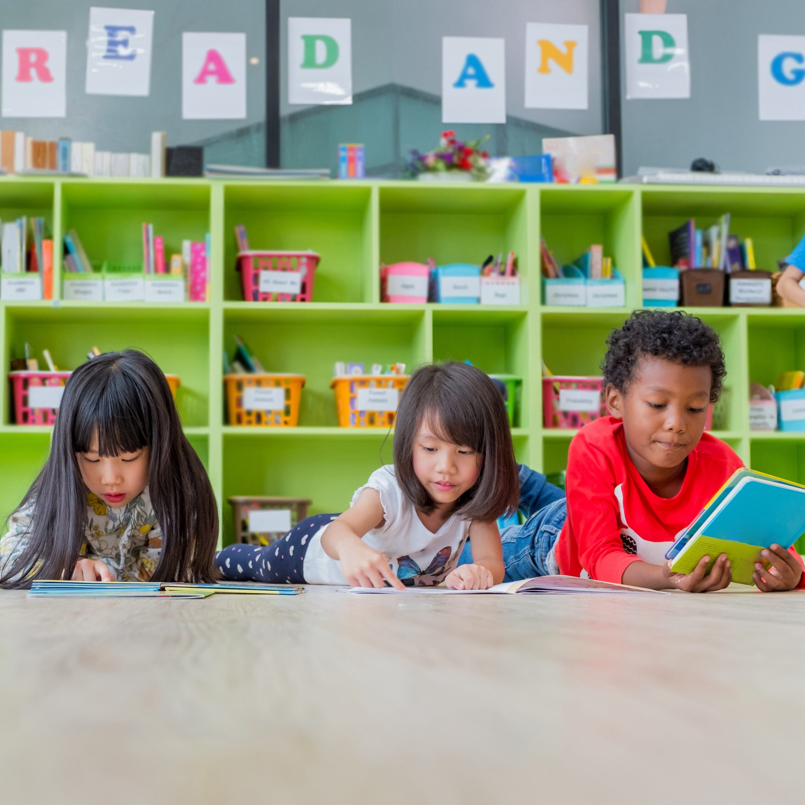 Group of diverse children laying on a classroom floor reading books.