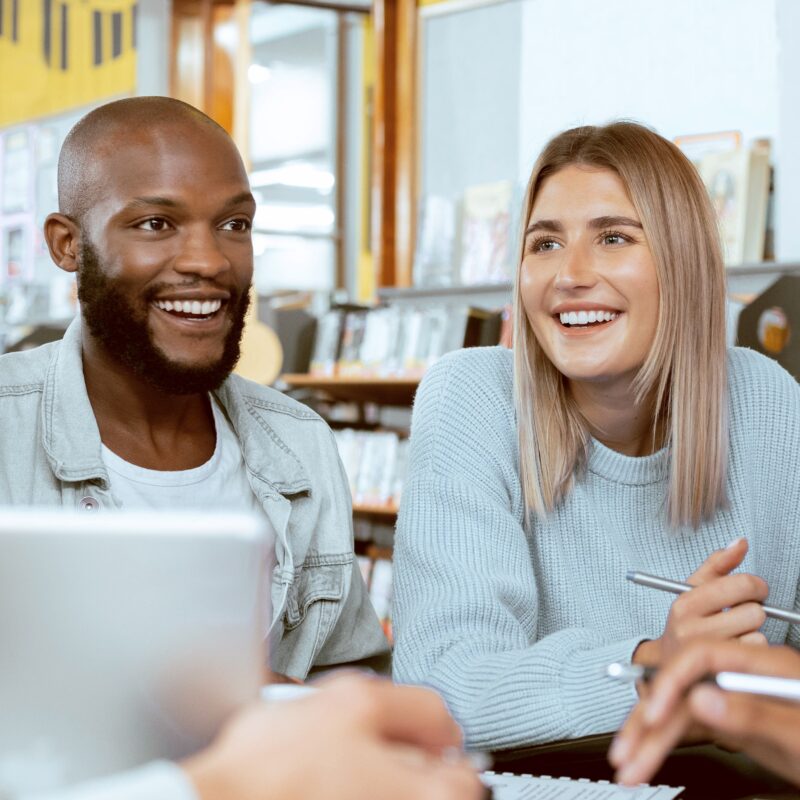 Two young professionals smiling and sitting at a table with laptops