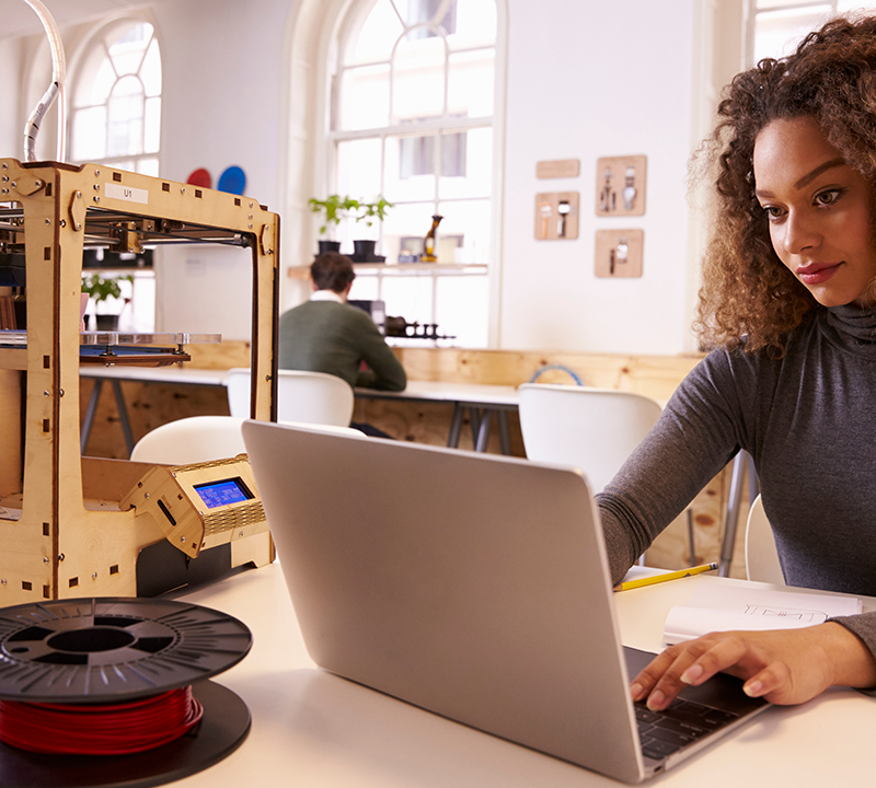 Photo of a young adult working with a laptop and 3D printer