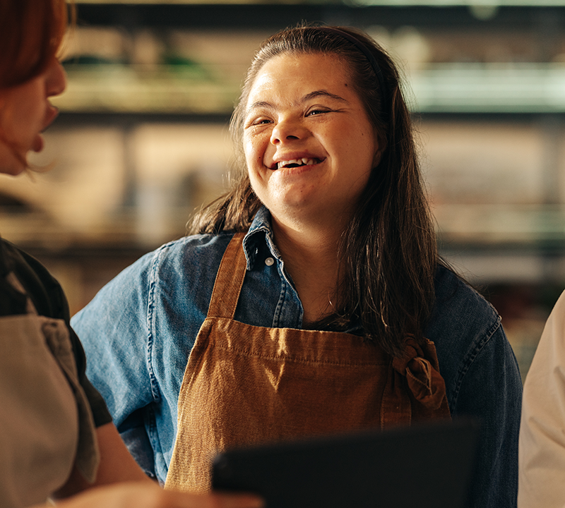 Photo of a woman with Down syndrome smiling and speaking to colleagues at a grocery store