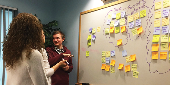 New Hampshire educators collaborating around a whiteboard with sticky notes on it, New Hampshire educators working together on a journey map, New Hampshire educators collaborating on chart paper with sticky notes, Photo of the four NH UDL Innovation Network annual reports displayed on a table