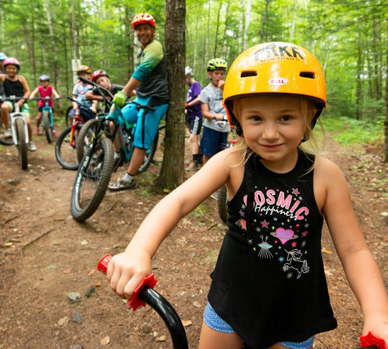 Photo of a group of children bike riding in the woods with adults