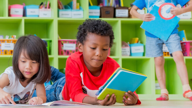 A bright classroom with colorful bins of books and supplies and a reading group of young students.